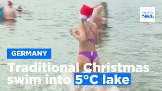 Traditional Christmas swim into freezing lake in Berlin with swimmers dressed in Santa hats [upl. by Leirea]