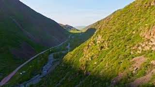 green slopes of mountain ravine with dirt road and small creek during spring evening slow aerial [upl. by Onit]